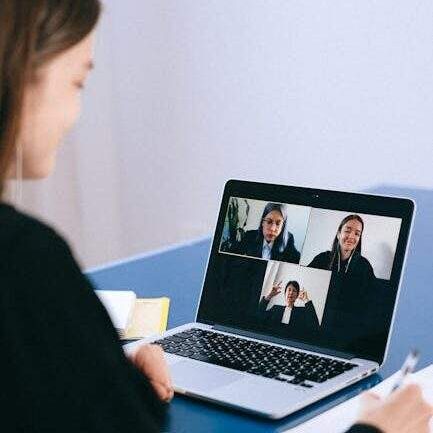 A woman participates in a virtual meeting with colleagues via video call on a laptop.